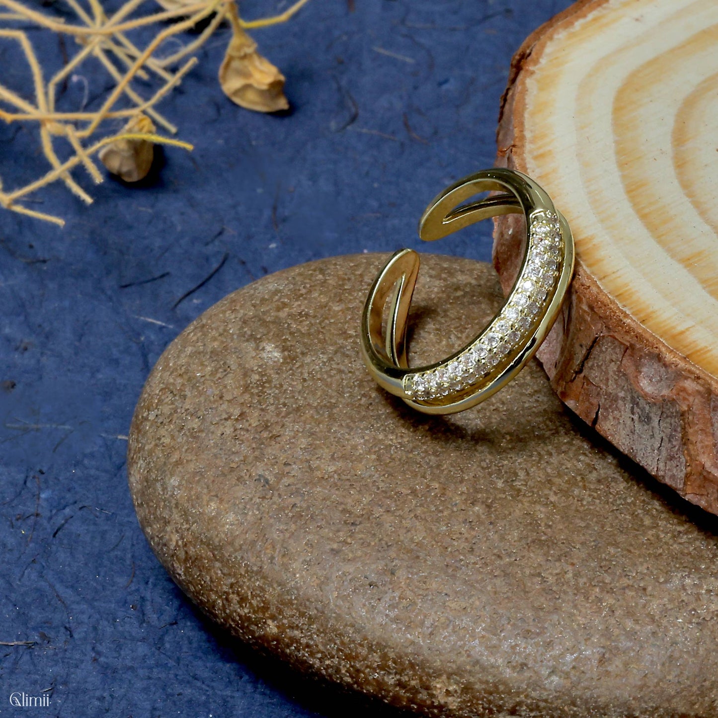 Adjustable gold statement ring with sparkling stones displayed on natural stone and wood background