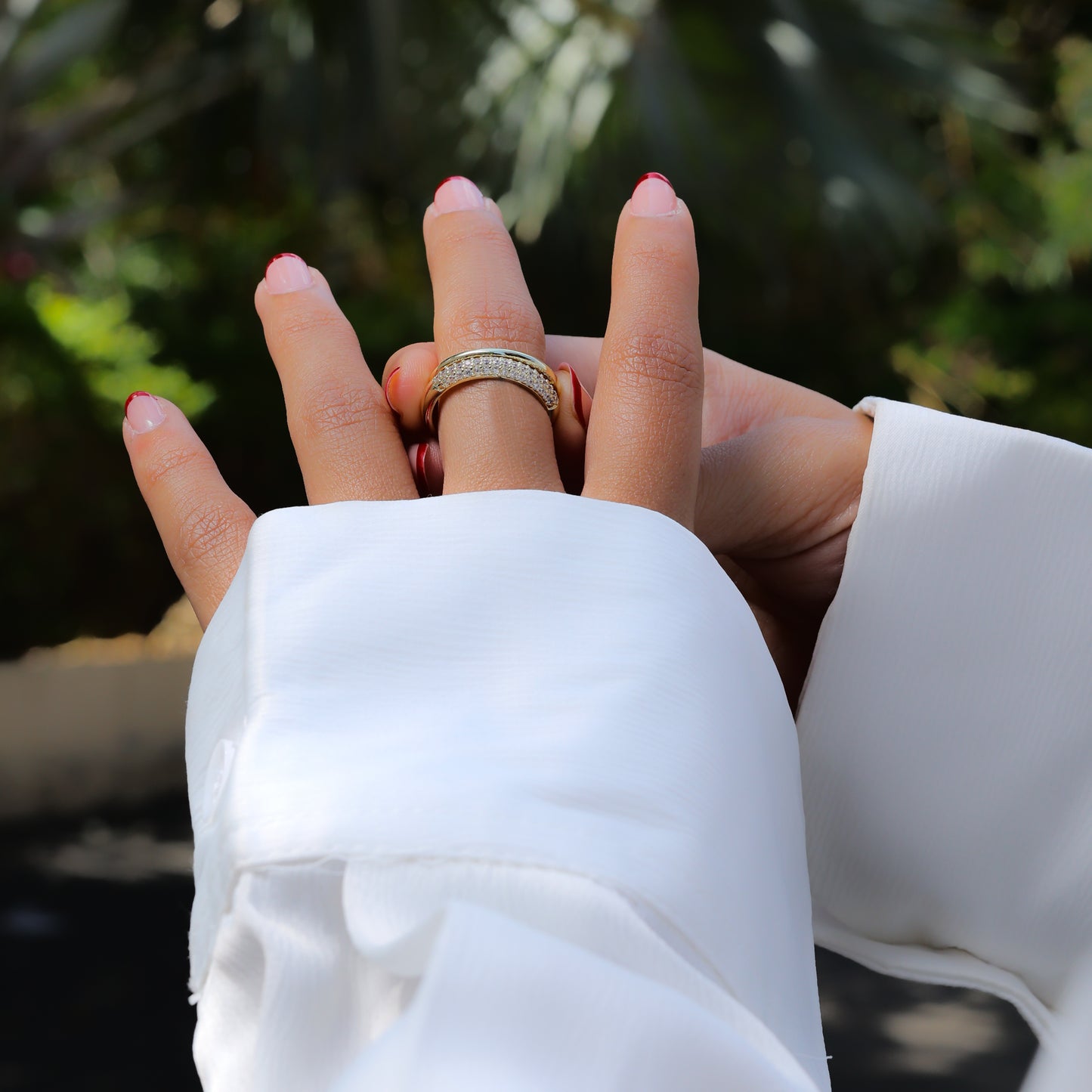 Closeup of hands wearing an adjustable gold statement ring with white stones and white sleeves outdoors