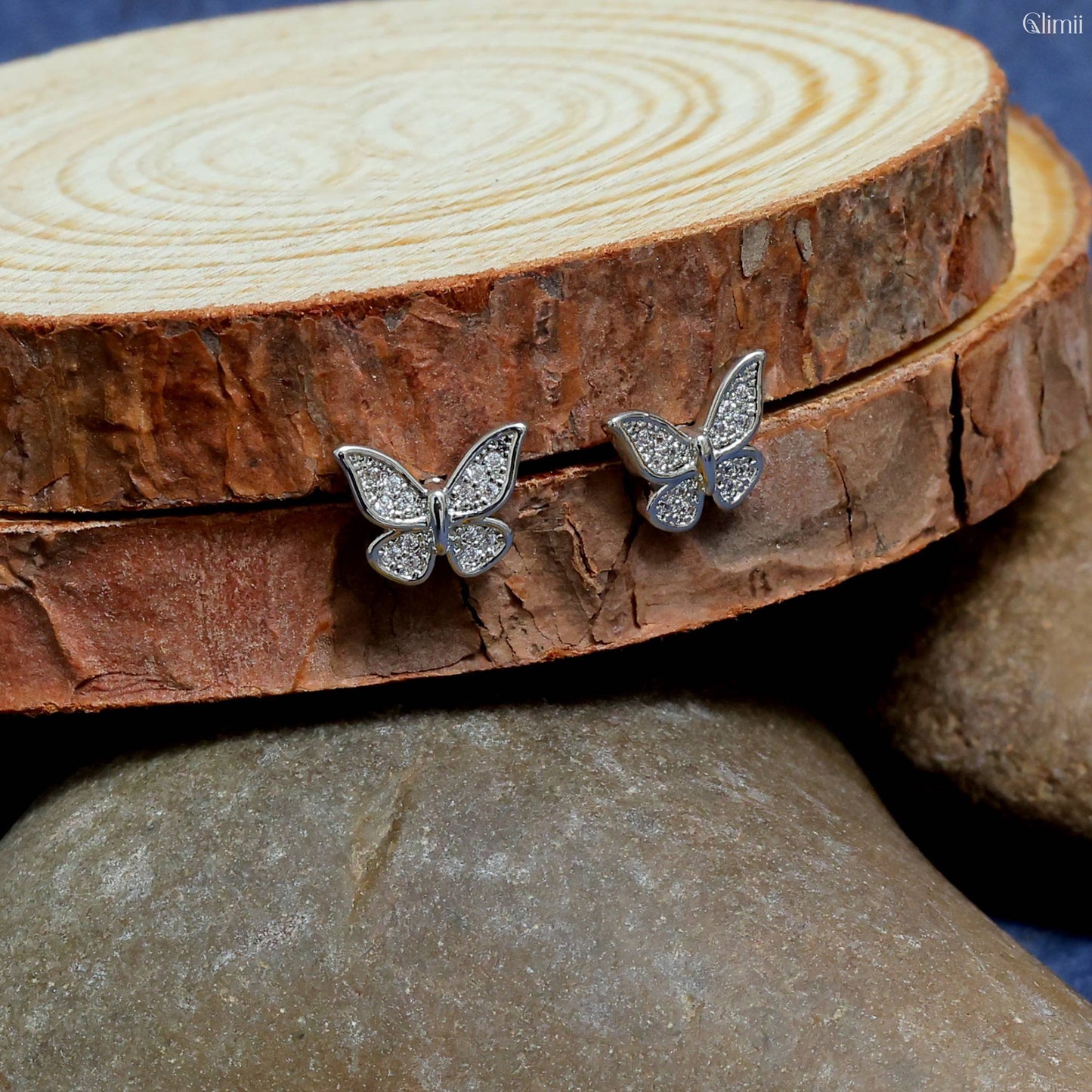 Glimii butterfly stud earrings with sparkling stones displayed on natural wood and stone background