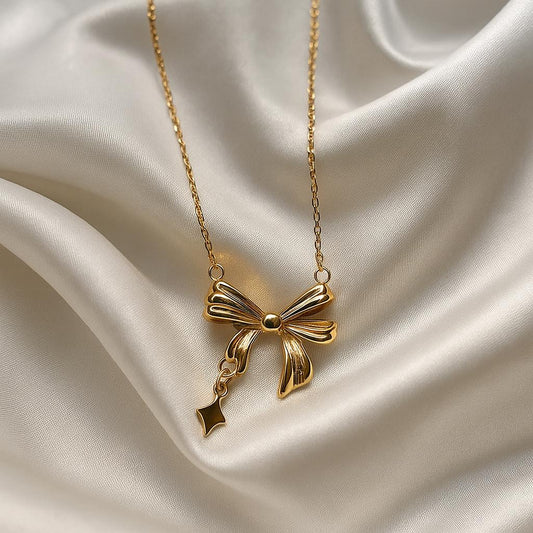 Glimii elegant gold bow necklace with delicate chain displayed on smooth silk fabric