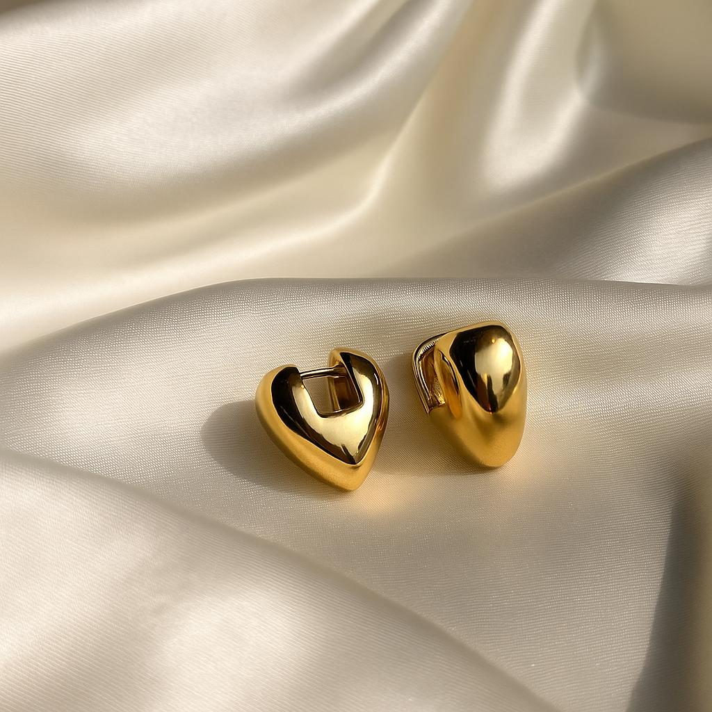 Glimii gold heart hoop earrings placed on smooth cream satin fabric background