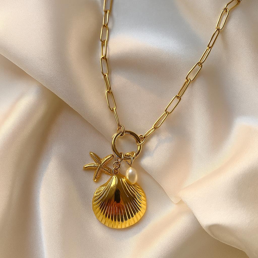 Glimii gold plated sea shell necklace with starfish charm and pearl on chain over satin fabric