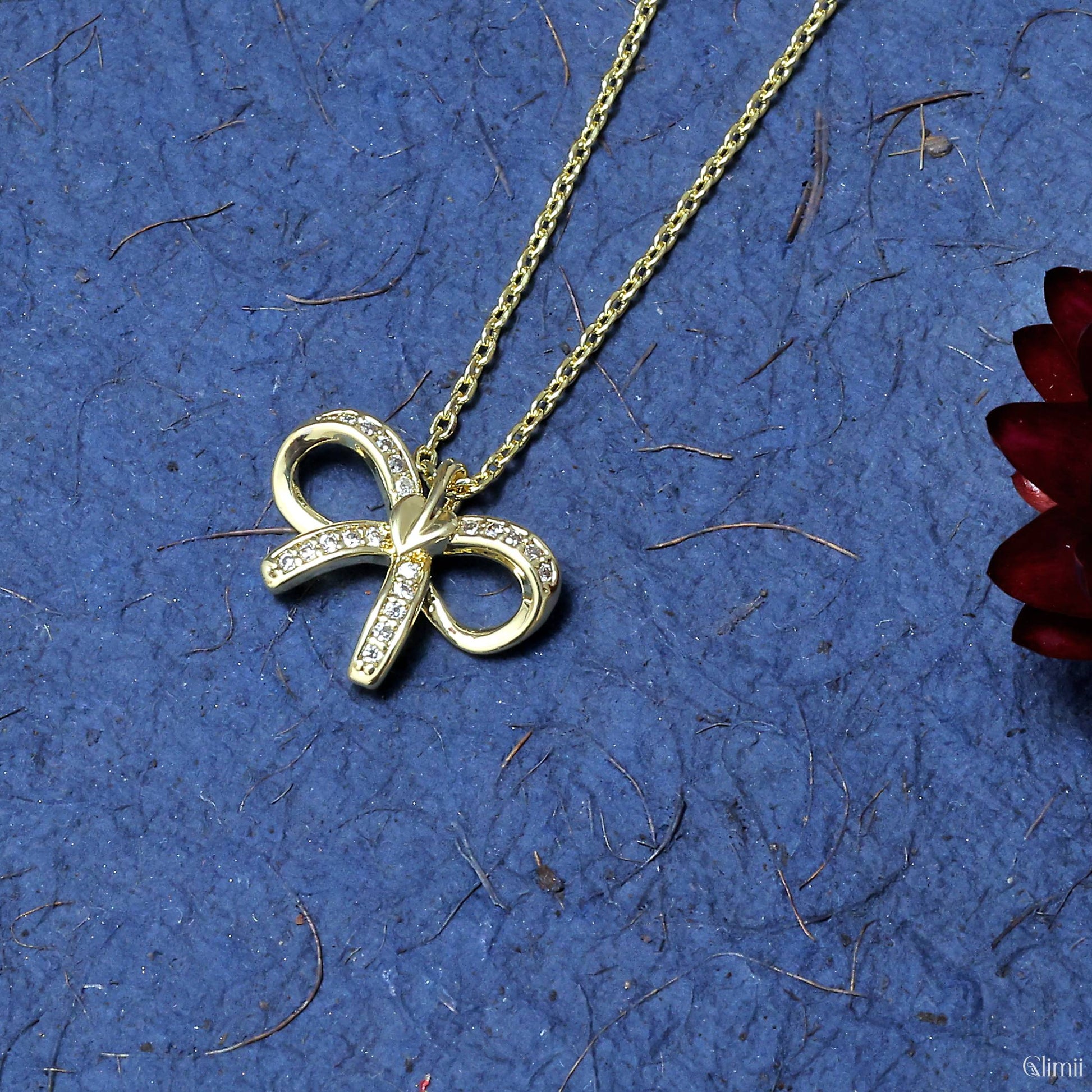 Glimii Korean style bow necklace in gold with crystal accents on a blue textured background