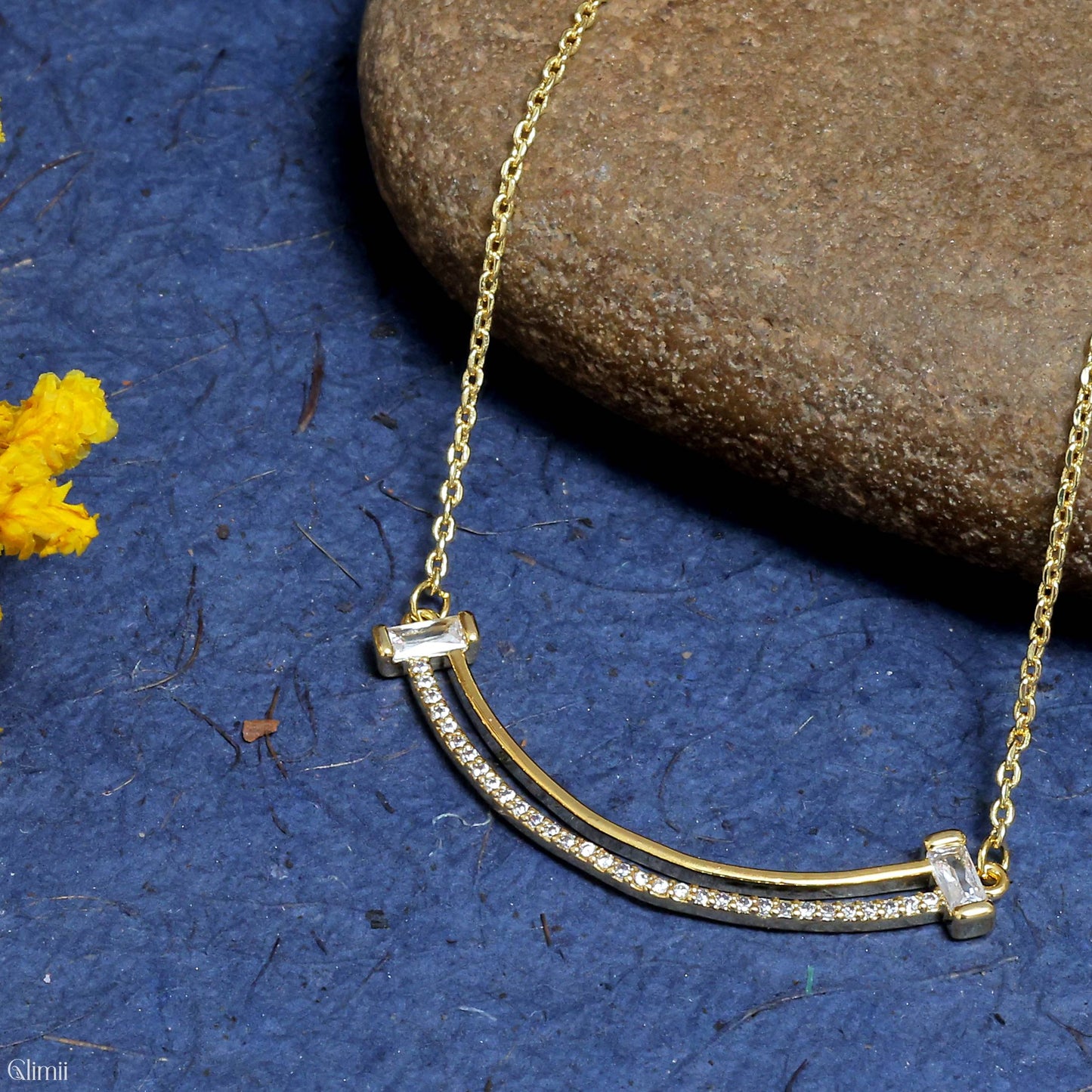 Glimii gold curved bar layered aesthetic necklace with embedded crystals on a blue textured background