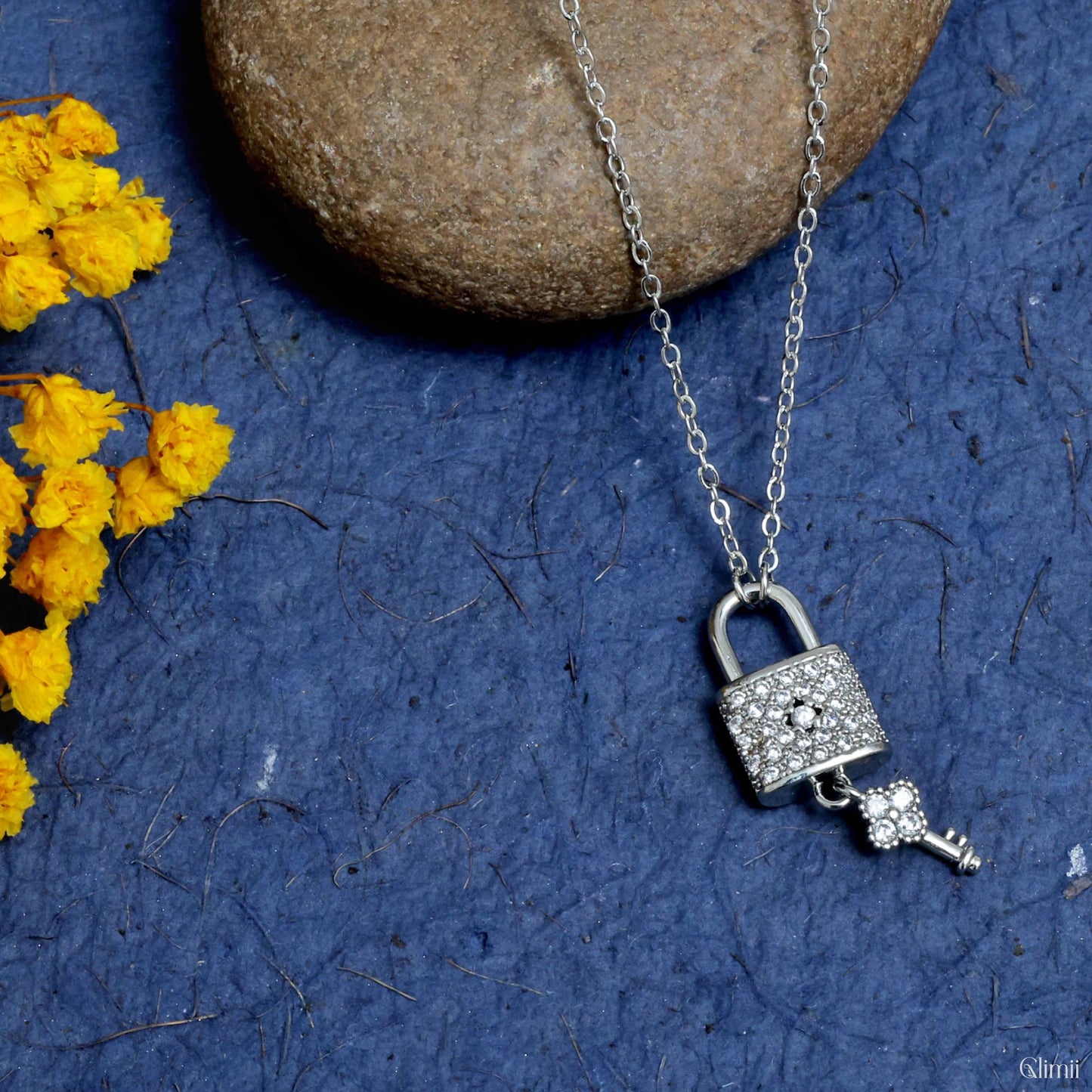 Glimii lock and key necklace with silver chain and crystal-studded pendant on blue background