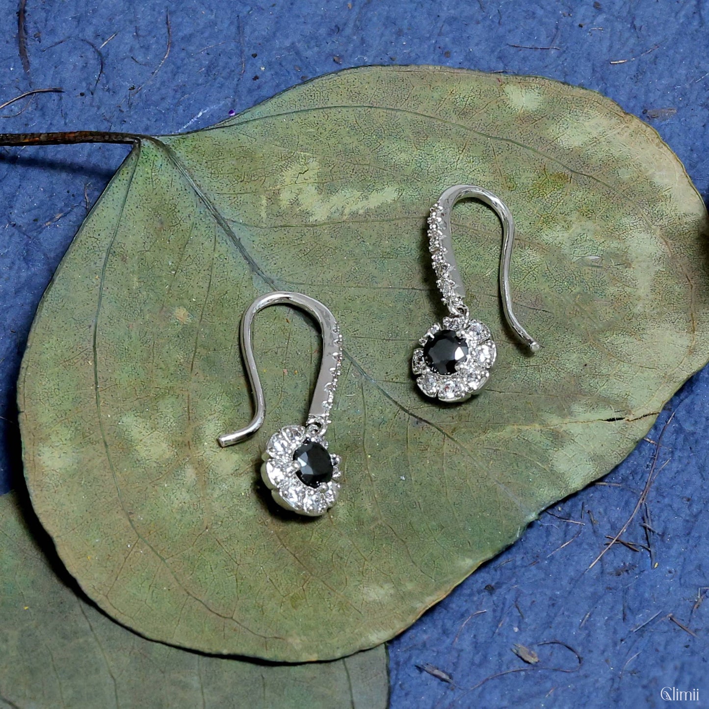 Glimii minimalist black drop earrings with silver and clear crystal accents on green leaf background