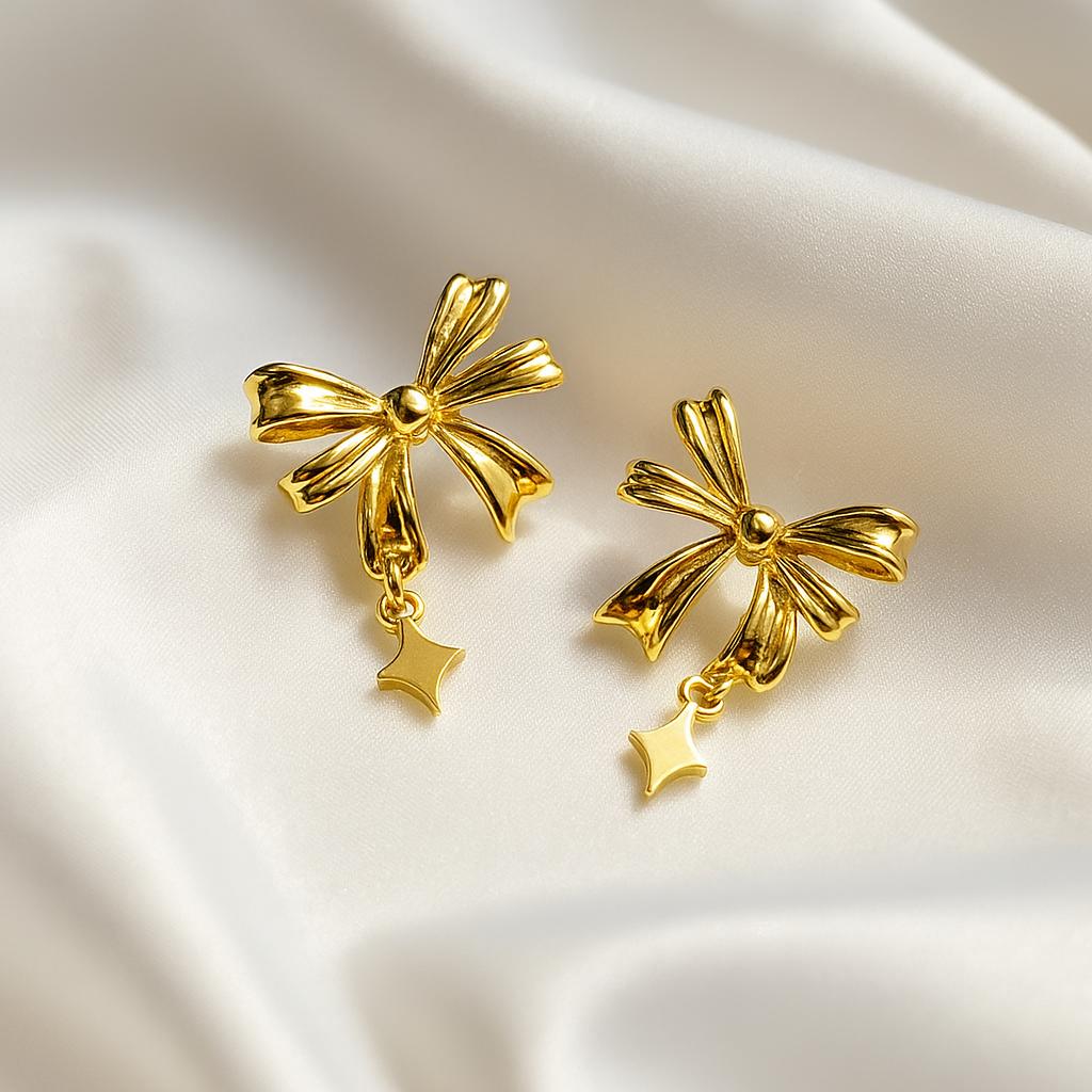 Gold bow shaped minimalist Korean style earrings with dangling star charm on white fabric