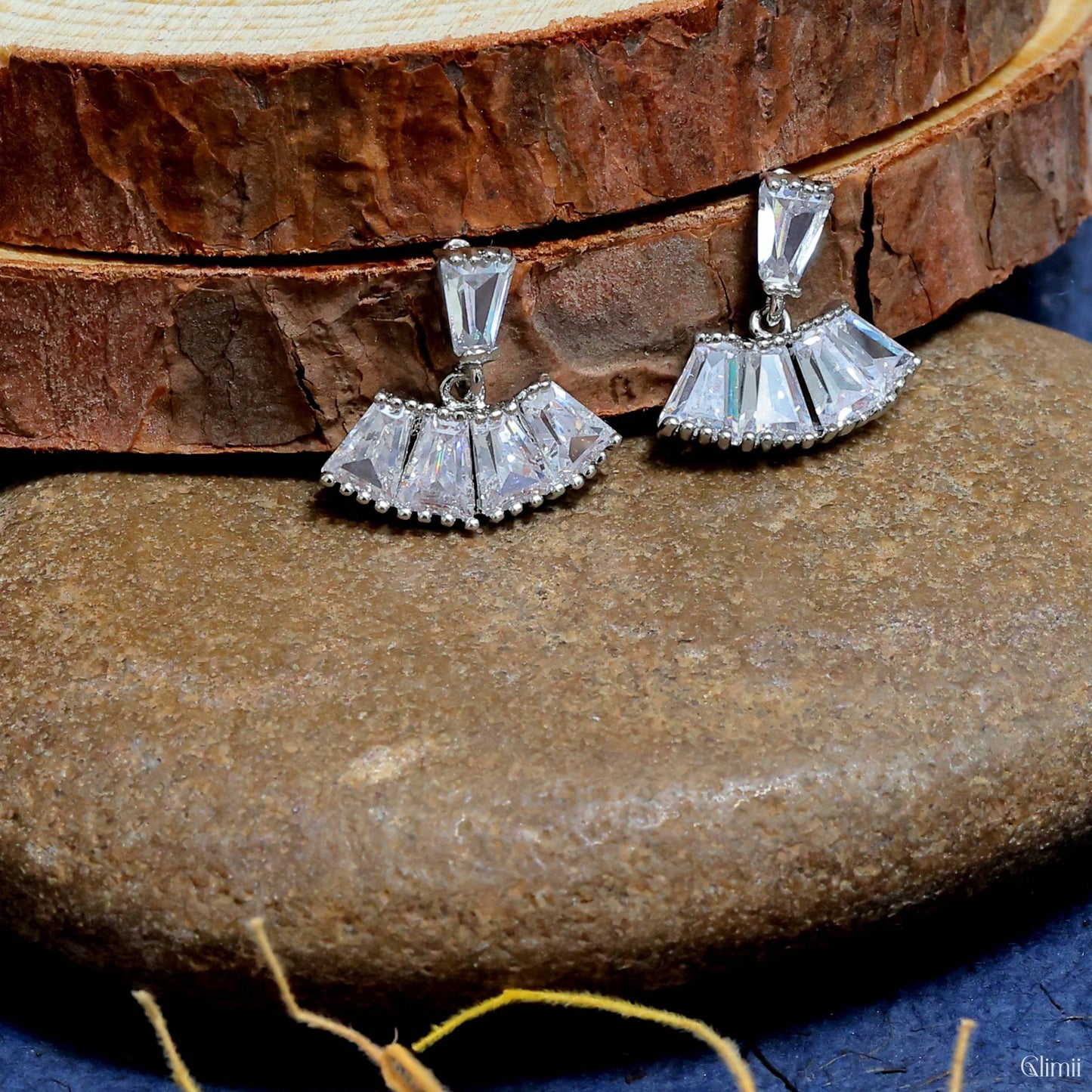 Glimii minimalist stainless steel earrings with clear geometric crystals displayed on natural stone and wood