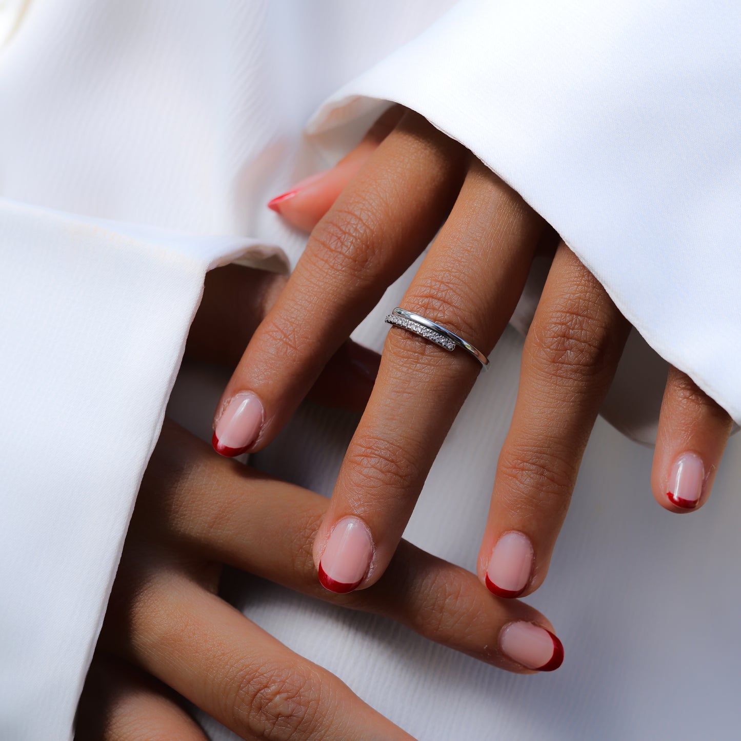 Glimii adjustable O statement ring on a hand with red French manicure and white fabric background