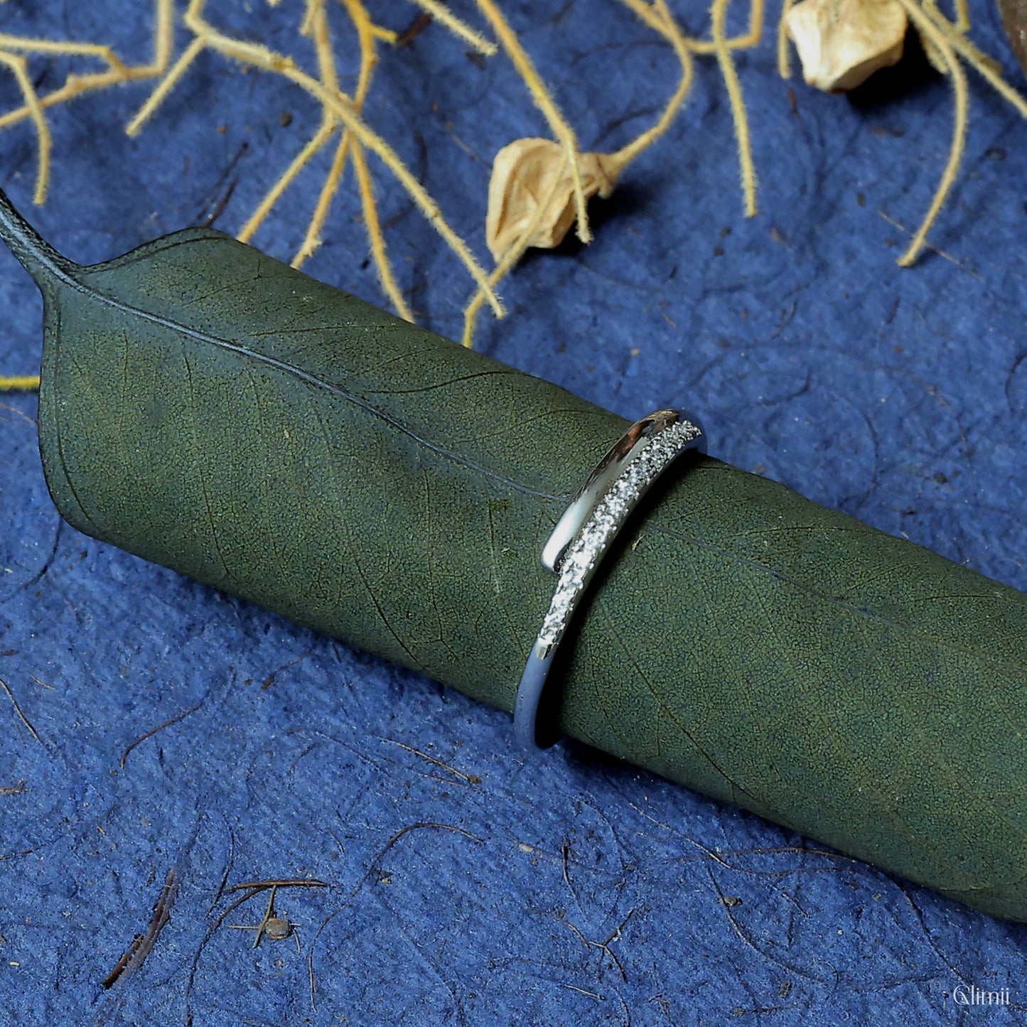Glimii adjustable O statement ring with silver textured design on green leaf and blue background