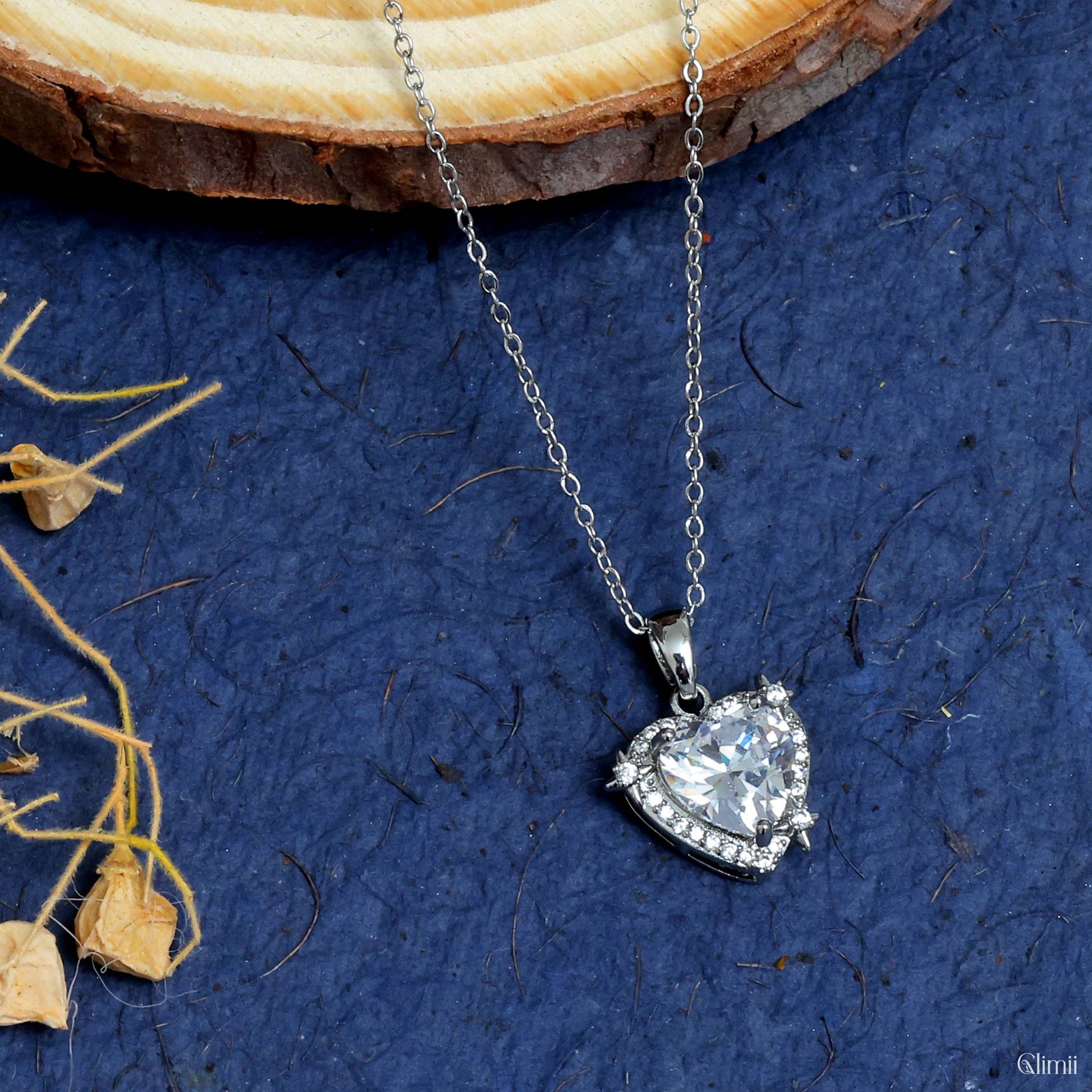 Glimii minimalist heart pendant necklace with silver chain and sparkling heart-shaped crystal on blue background
