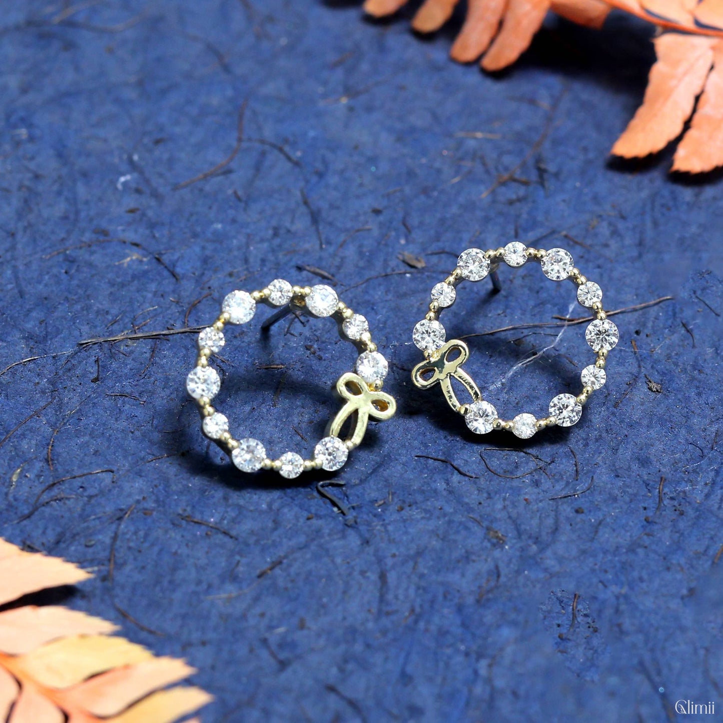 Glimii stainless steel hoop earrings with sparkling crystals and small bow accents on blue textured background