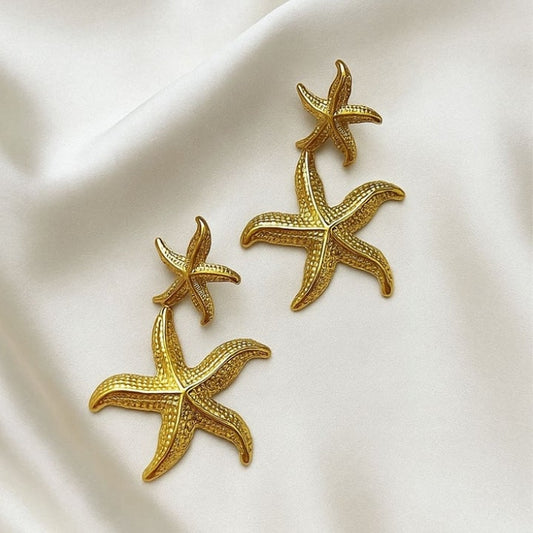 Glimii starfish gold dangle earrings featuring textured double starfish design on white fabric
