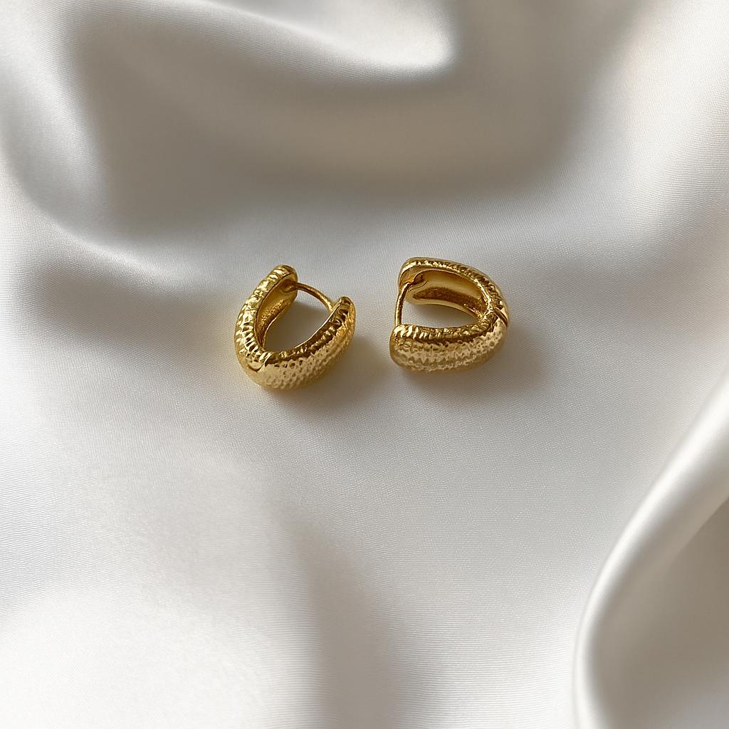 Glimii textured gold hoop earrings displayed on a smooth white satin fabric background
