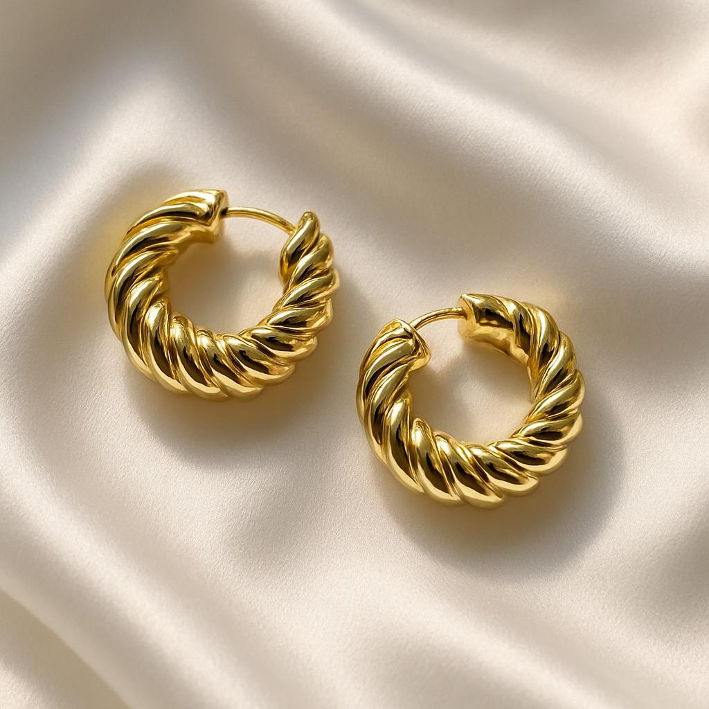 Glimii twisted gold hoop earrings with a bold twisted design on a silk fabric background