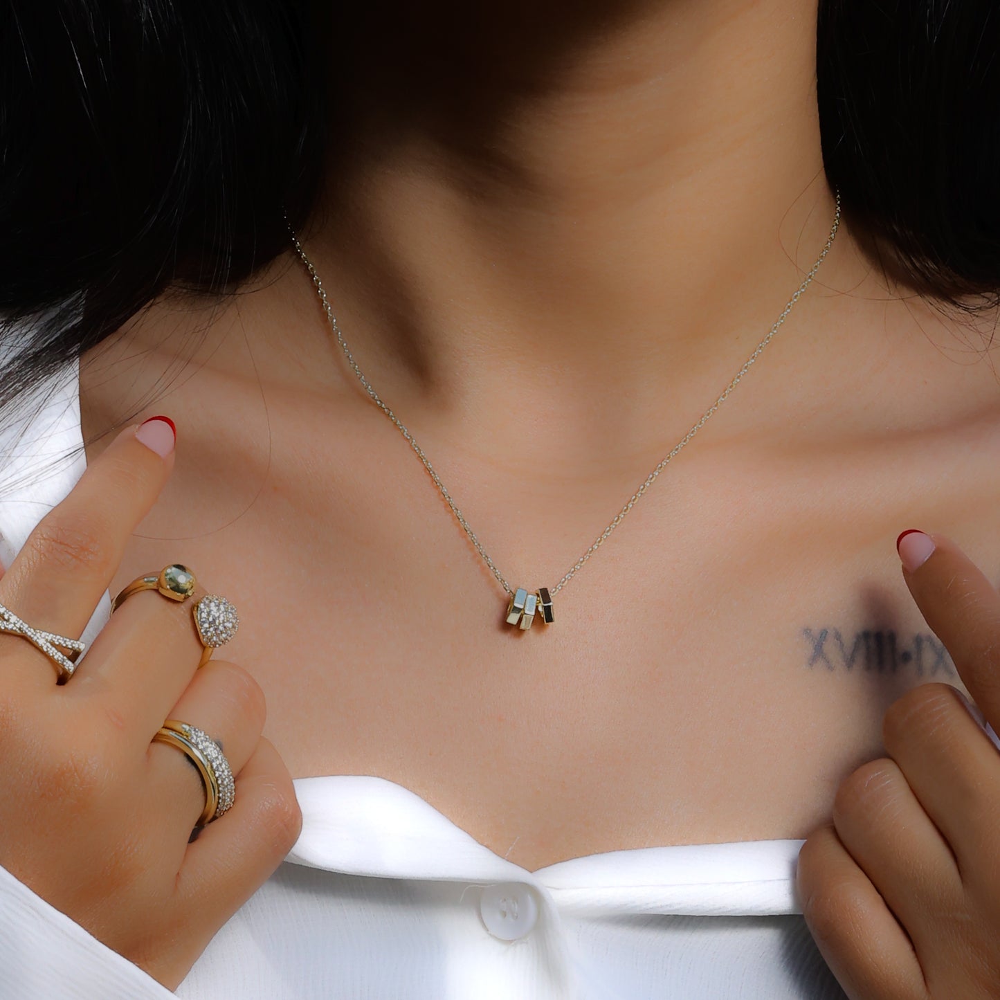 Glimii everyday aesthetic necklace with small geometric pendants worn with gold rings and white top