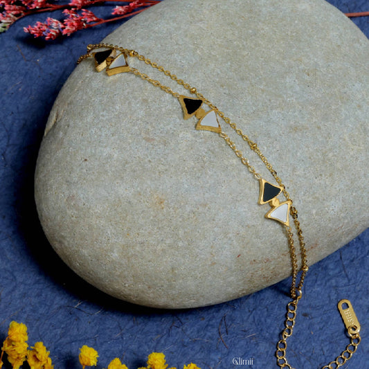 Delicate gold layering bracelet by Glimii with black and white triangle charms on a stone background