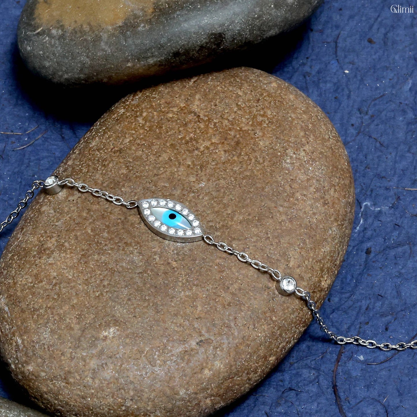 Glimii everyday evil eye charm bracelet with silver chain and blue eye charm on natural rocks