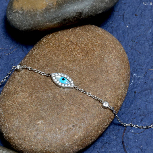 Glimii everyday evil eye charm bracelet with silver chain and blue eye charm on natural rocks