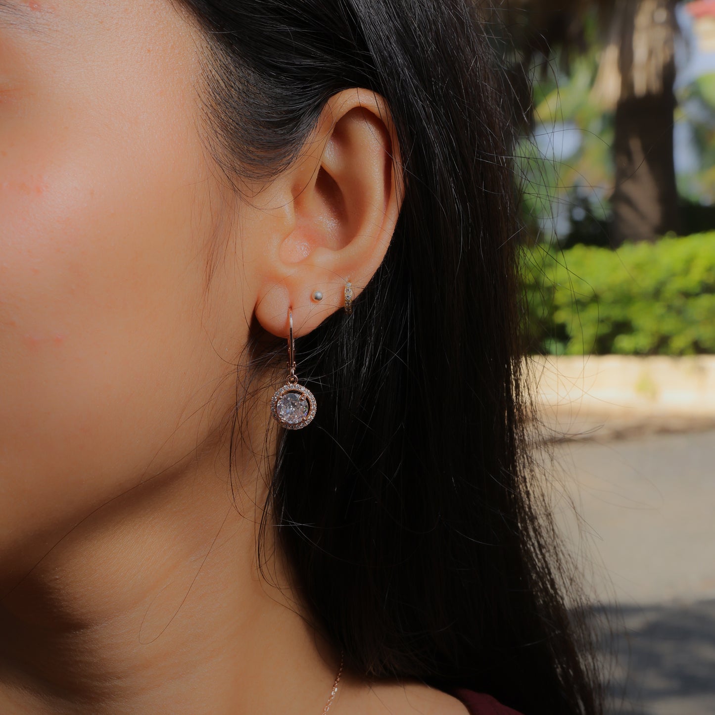Glimii dainty stainless steel earrings with a sparkling round pendant worn on a woman's ear outdoors
