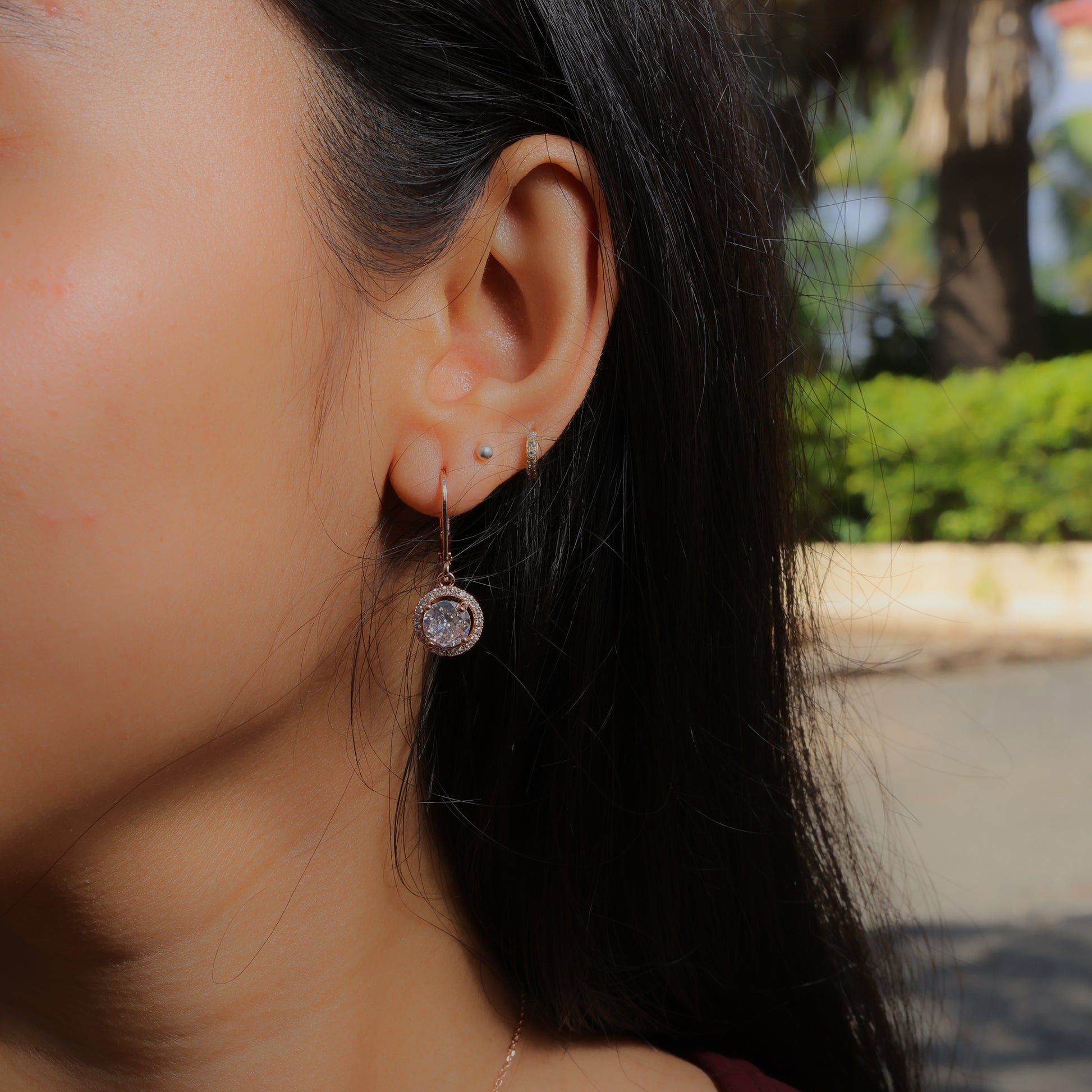 Glimii dainty stainless steel earrings with a sparkling round pendant worn on a woman's ear outdoors