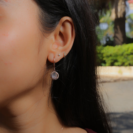 Glimii dainty stainless steel earrings with a sparkling round pendant worn on a woman's ear outdoors