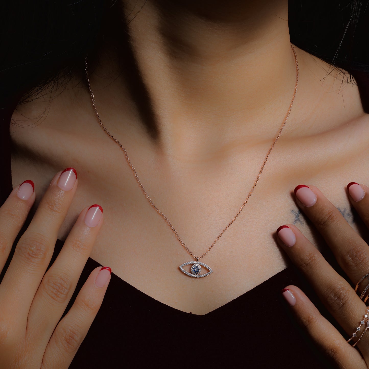 Glimii evil eye necklace with delicate chain worn on neck against dark background