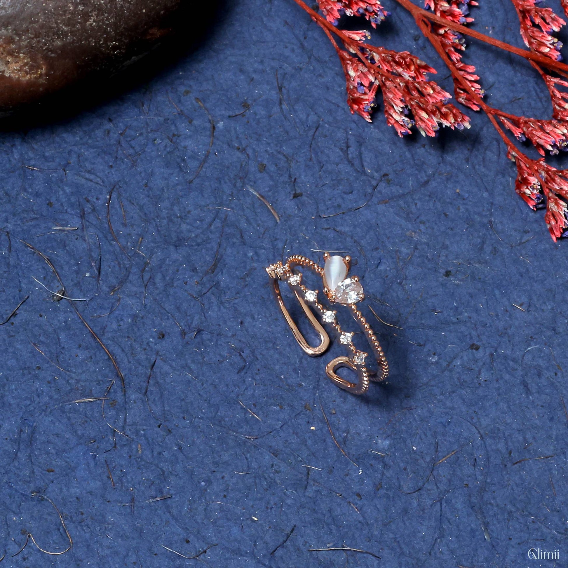 Glimii minimalist butterfly ring in rose gold with delicate design and small gemstone accents on blue textured background