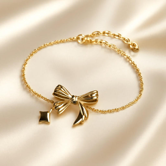 Glimii gold bow charm bracelet with delicate chain and small dangling star charm on satin background