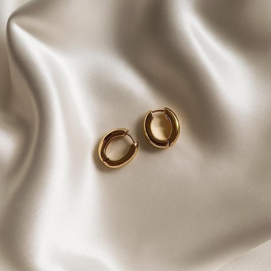 Glimii Korean style crescent earrings in polished gold-tone metal on smooth beige fabric