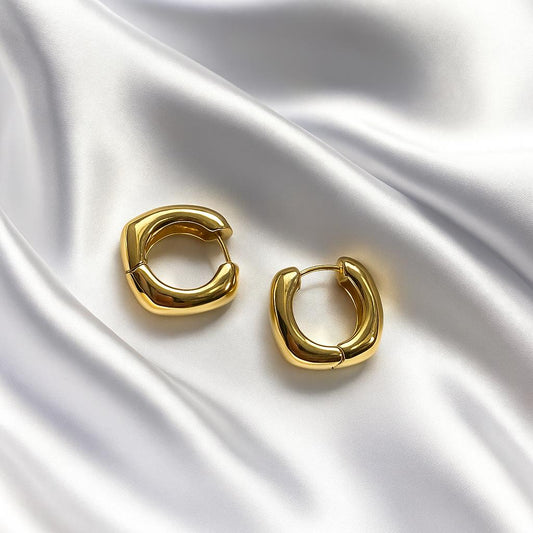 Glimii minimalist broad hoop earrings in shiny gold displayed on silky white fabric