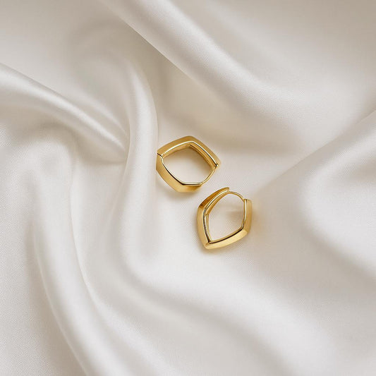 Glimii gold V shape hoop earrings resting on smooth white fabric background