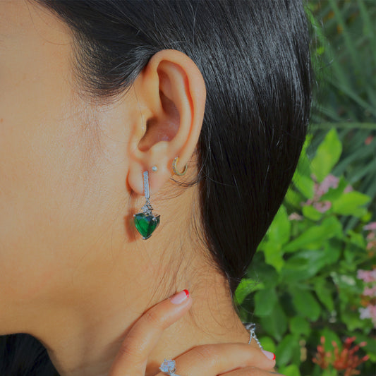Close-up of Glimii green heart drop earrings worn on ear with natural outdoor background