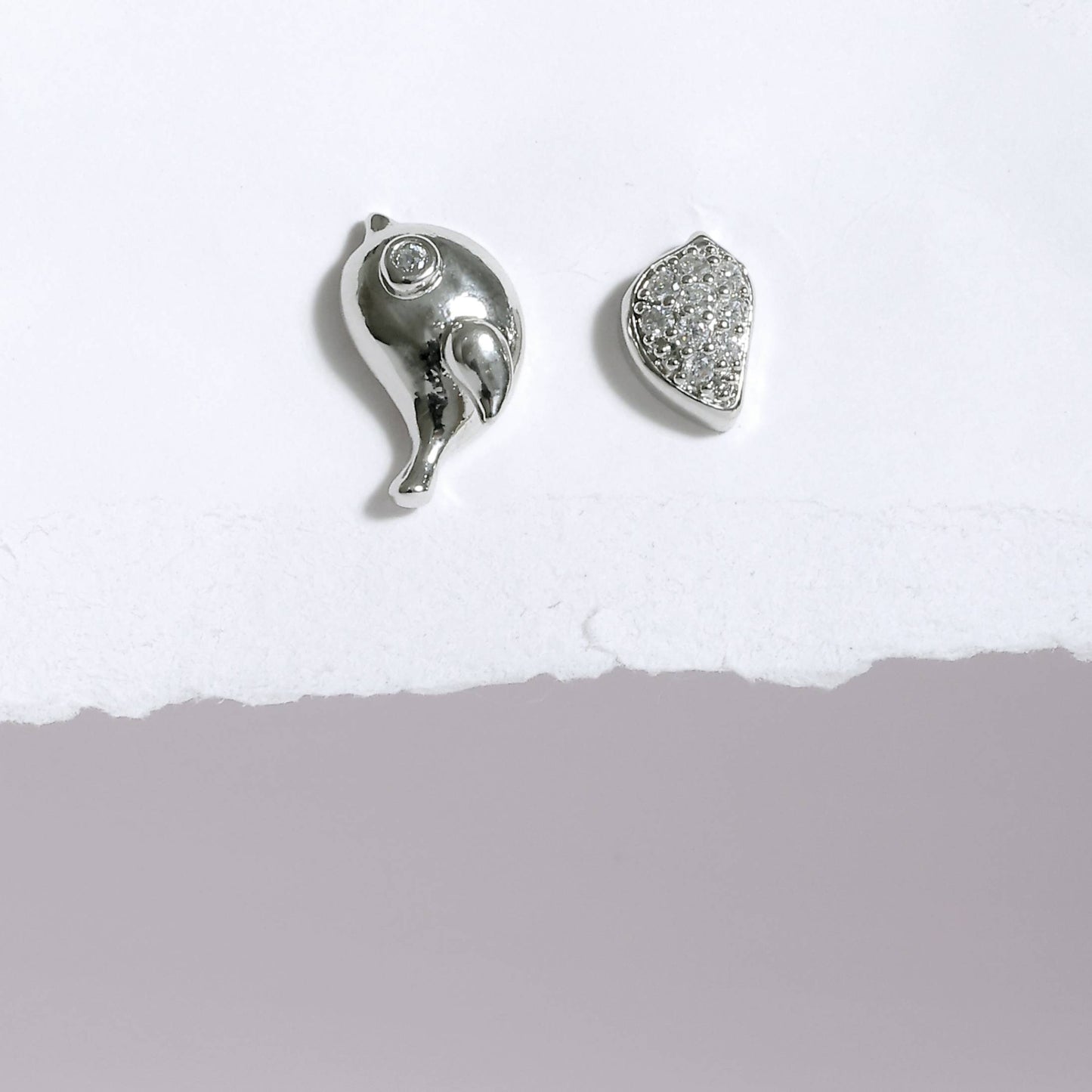 Silver korean style bird earrings with one bird-shaped and one crystal-studded design on white background