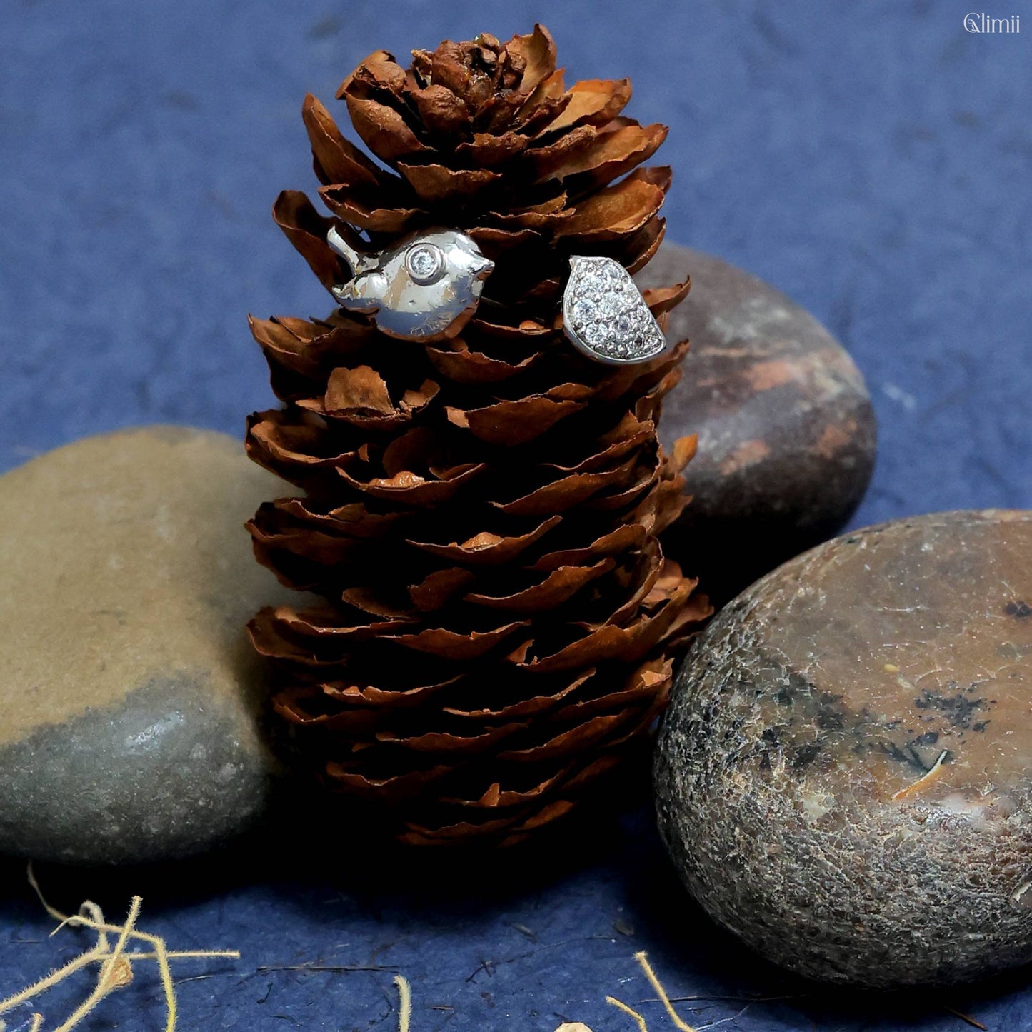 Glimii silver korean style bird earrings displayed on a pine cone with natural stone background
