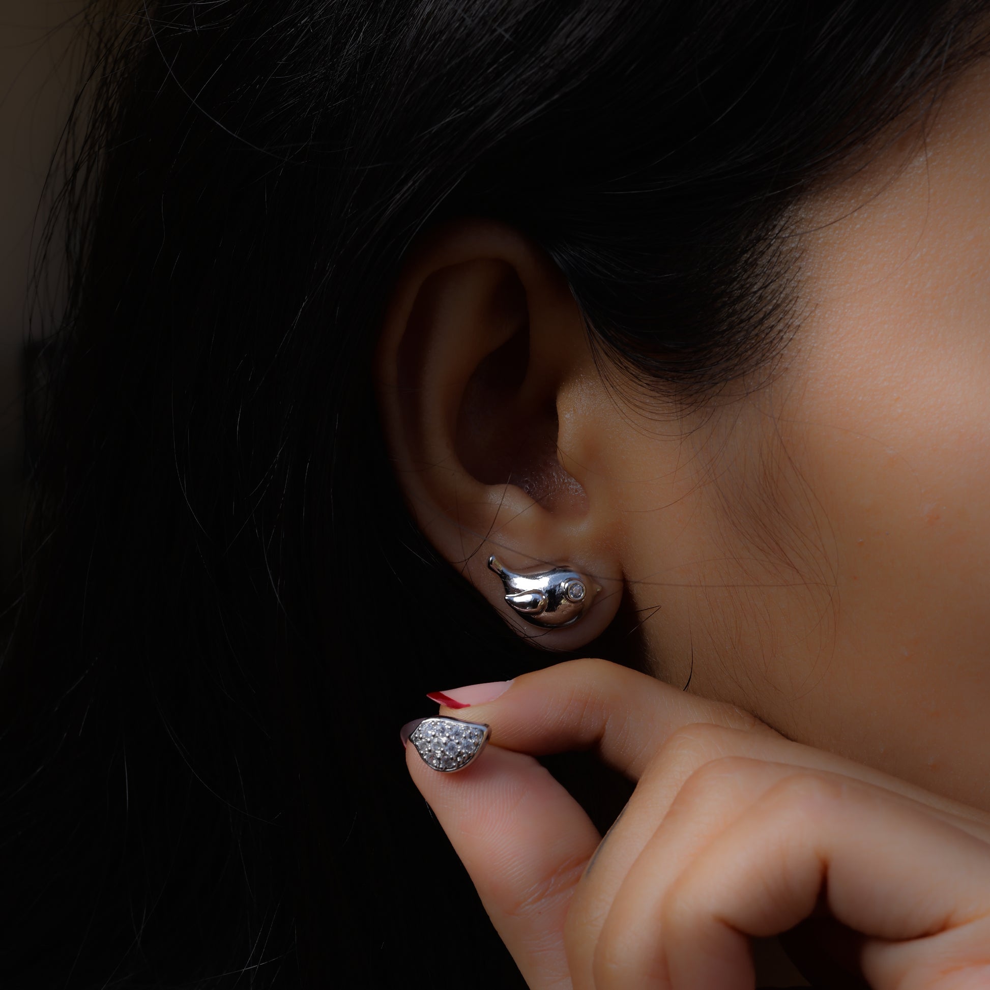 Silver korean style bird earrings worn on ear with hand holding glittery nail close up