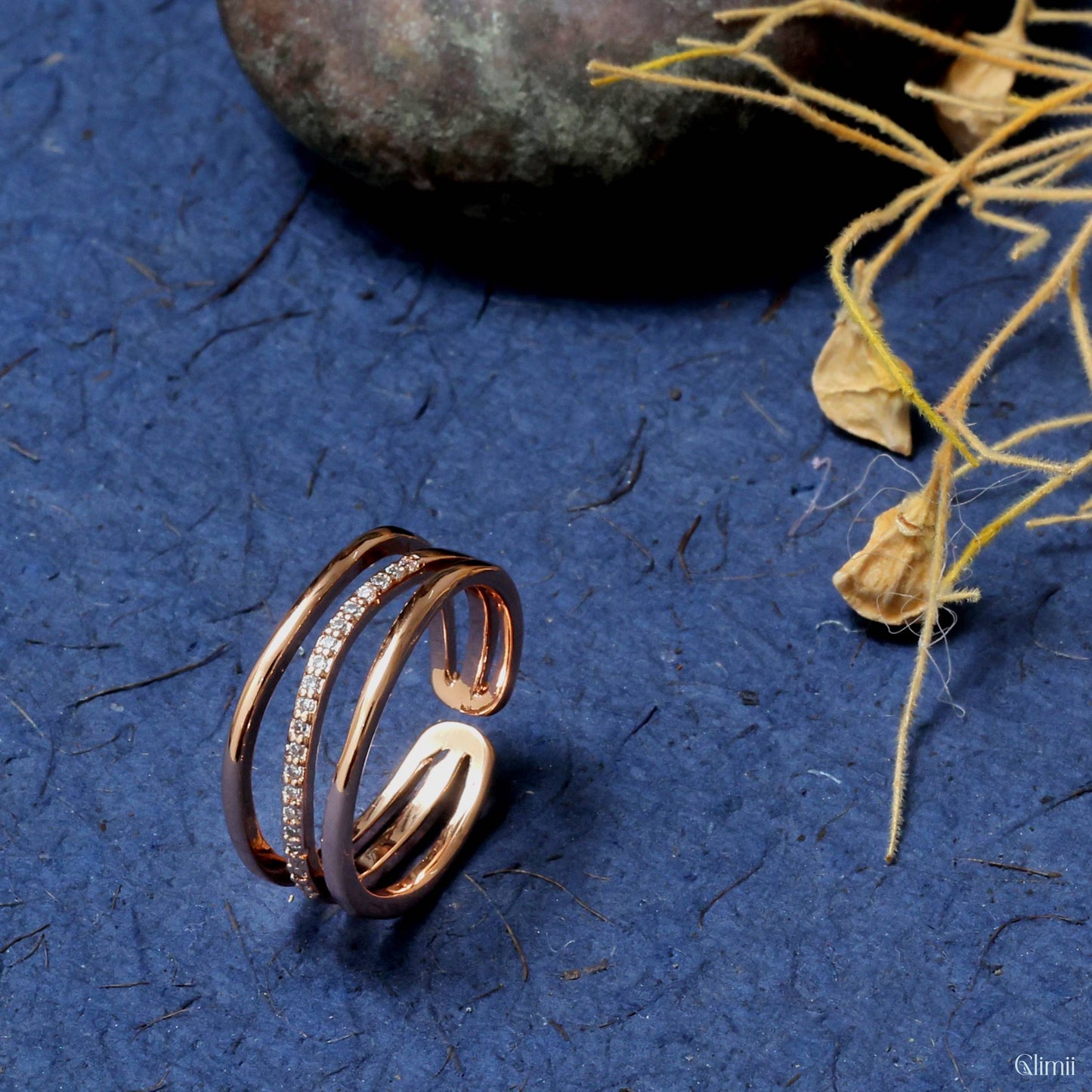 Elegant rose gold Korean style jewelry ring with embedded small crystals on blue textured background