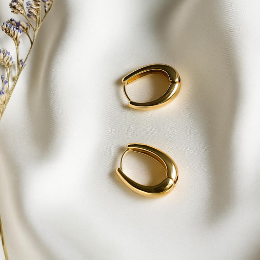 Minimalist gold hoop earrings by Glimii on a soft white fabric with dried flowers