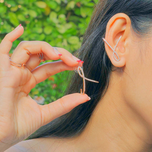 Glimii minimalist knot earrings worn on ear and held by hand in natural outdoor background