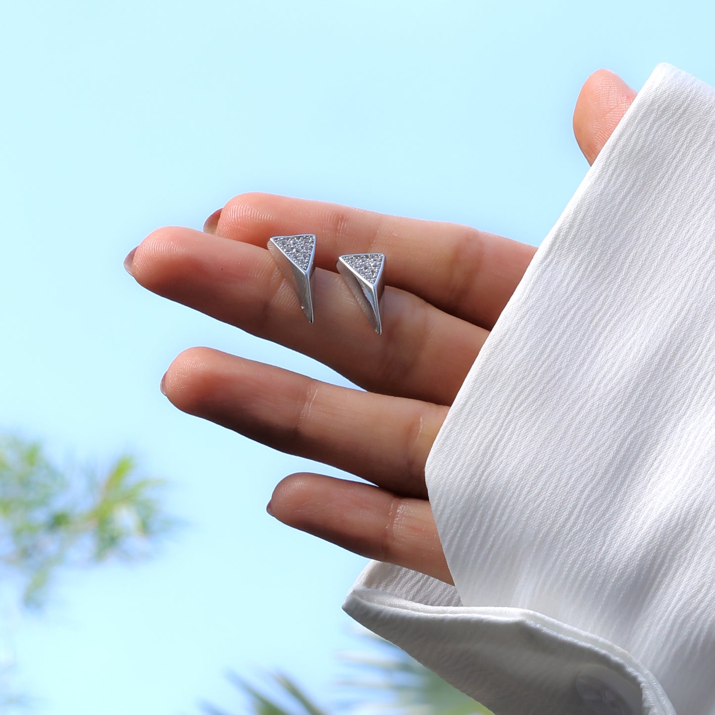Glimii modern diamond accent jewelry triangular silver stud earrings held in hand with white sleeve