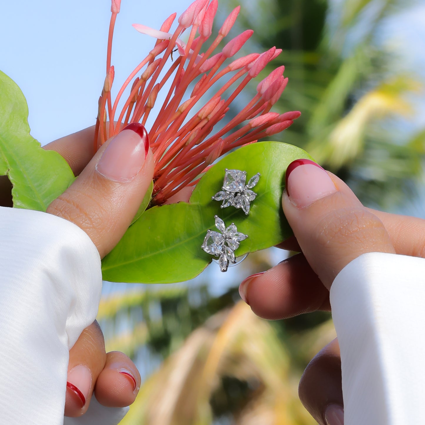 Glimii delicate everyday earrings shaped like flowers held on a green leaf with a tropical background