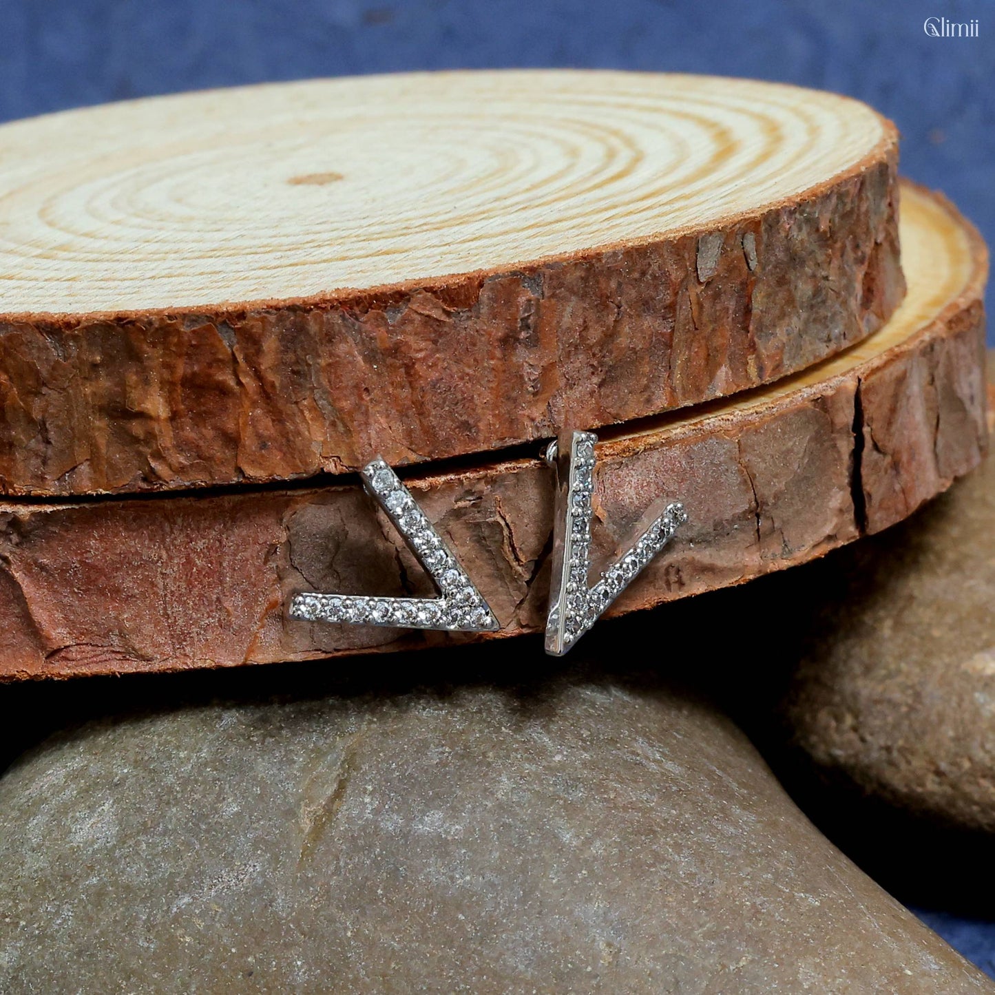 Glimii stainless steel stud earrings with a modern V-shaped design and embedded crystals on natural wood background