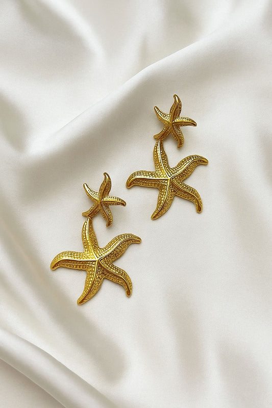 Glimii starfish gold dangle earrings featuring textured double starfish design on white fabric