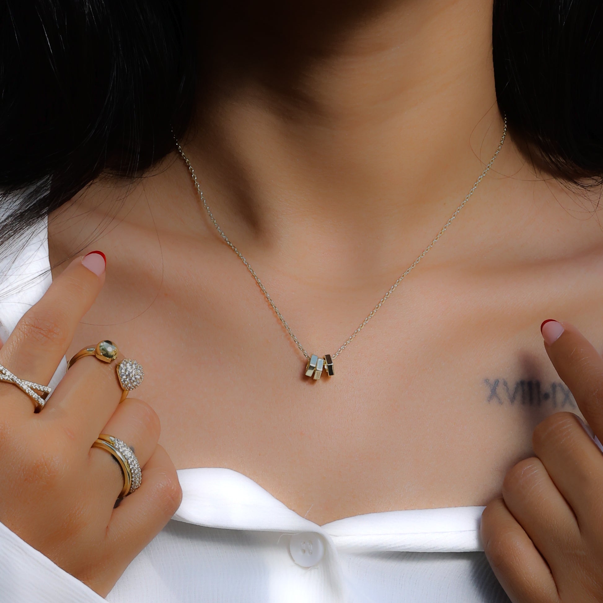 Glimii everyday aesthetic necklace with small geometric pendants worn with gold rings and white top