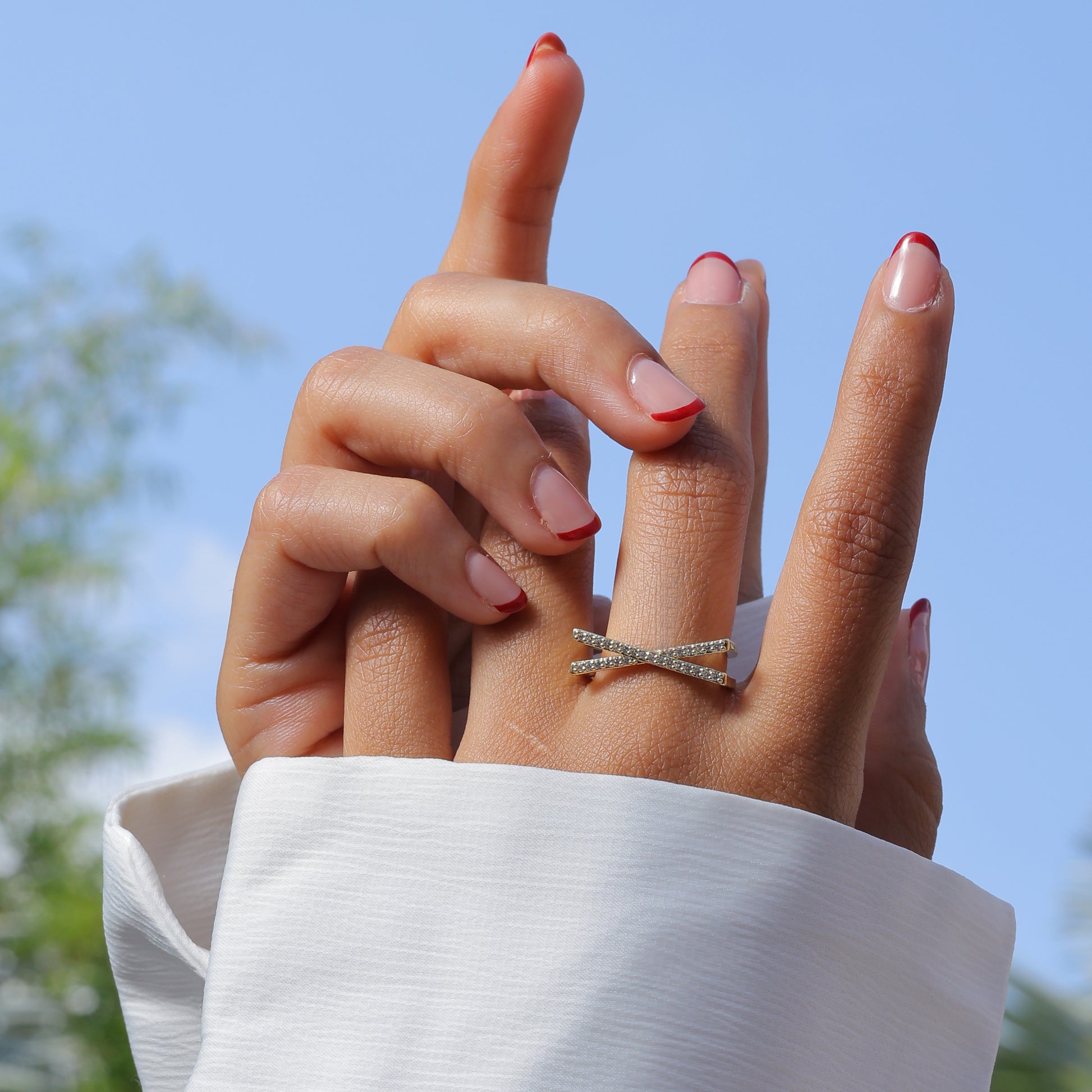 Elegant Korean style jewelry ring with crisscross design worn on finger against blue sky background